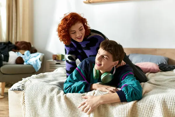 Beau jeune homme avec écouteurs couché à côté de sa petite amie rousse aimante sur le lit — Photo de stock