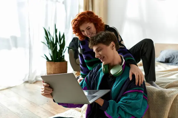 Hermosa mujer alegre en traje acogedor sentado en la cama y pasar tiempo con su novio en el ordenador portátil - foto de stock