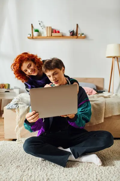 Atractivo alegre joven pareja en vibrante ropa elegante pasar tiempo en el ordenador portátil juntos en casa - foto de stock