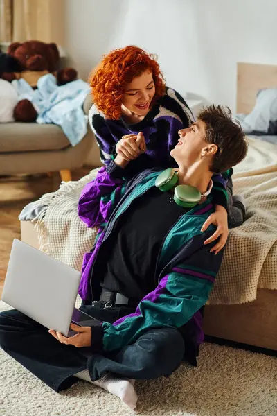 Young loving cheerful couple in trendy clothes spending time at their laptop together on bed — Stock Photo