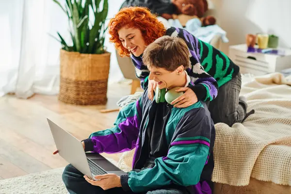 Handsome man relaxing next to his red haired girlfriend while spending time at laptop together — Stock Photo