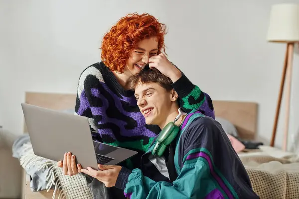 Добре виглядає радісна пара в яскравому одязі розважається під час серфінгу в Інтернеті на ноутбуці — стокове фото
