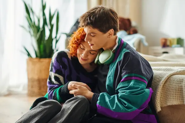 Hombre guapo con auriculares abrazando amorosamente a su hermosa novia pelirroja mientras está en casa - foto de stock