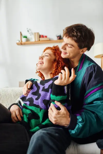 Beautiful cheerful couple in fashionable cozy clothes hugging each other while at home near bed — Stock Photo