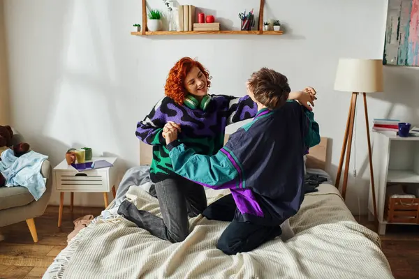Ansprechende fröhliche Freund und Freundin in lebendigen Kleidern haben viel Spaß auf dem Bett zu Hause — Stockfoto