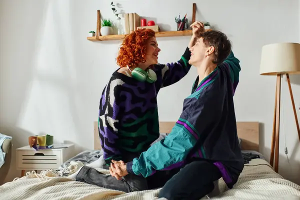 Buen aspecto pareja alegre apasionada en trajes vibrantes que se divierten mucho mientras están en la cama en su casa - foto de stock