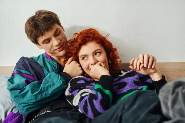 Cheerful attractive couple in vibrant trendy outfits hugging and laughing while in bed at home — Stock Photo