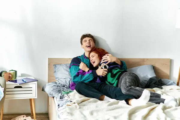 Alegre pareja atractiva en vívidos trajes de moda abrazando y riendo mientras que en la cama en casa - foto de stock
