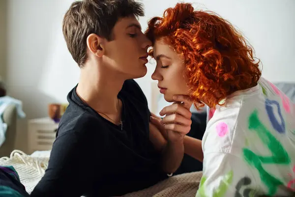 Good looking couple in fancy clothes sitting on bed together and preparing to kiss alluringly — Stock Photo