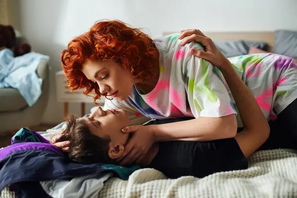 Радостная молодая пара в удобной домашней одежде готовится к соблазнительному поцелую, лежа на кровати вместе — стоковое фото