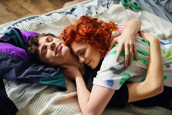 Attractive cheerful couple in cozy vibrant homewear hugging lovingly while lying on bed at home — Stock Photo