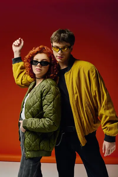 Appealing fashionable couple in stylish clothes with sunglasses posing on red backdrop together — Stock Photo