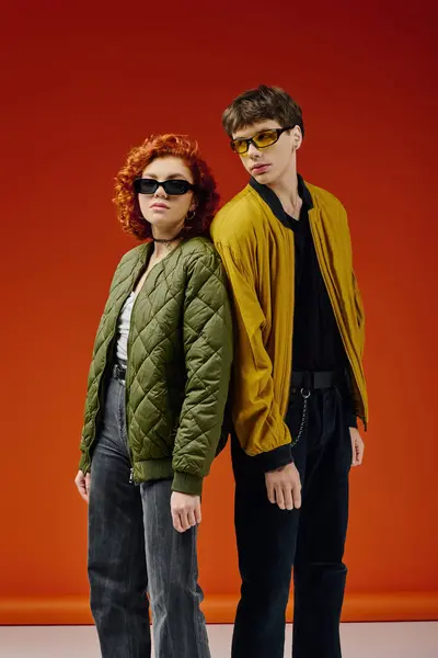 Aimant couple attrayant dans des vêtements à la mode avec des lunettes de soleil élégantes posant sur fond rouge — Photo de stock