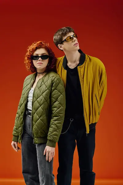 Стильна приваблива пара в модному вбранні з сонцезахисними окулярами позує разом на червоному тлі — стокове фото