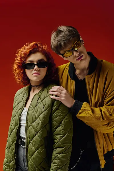 Attraktives modisches Paar mit trendiger Sonnenbrille in kuscheliger Kleidung posiert gemeinsam auf rotem Hintergrund — Stockfoto
