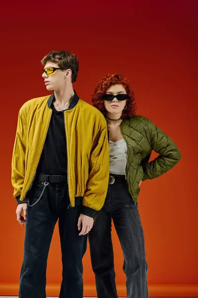 Attraktives stylisches Paar mit cooler Sonnenbrille in kuscheliger Kleidung posiert gemeinsam auf rotem Hintergrund — Stockfoto