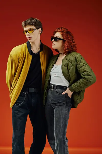 Schönes modisches Paar mit schicker Sonnenbrille in kuscheliger Kleidung posiert auf rotem Hintergrund zusammen — Stockfoto
