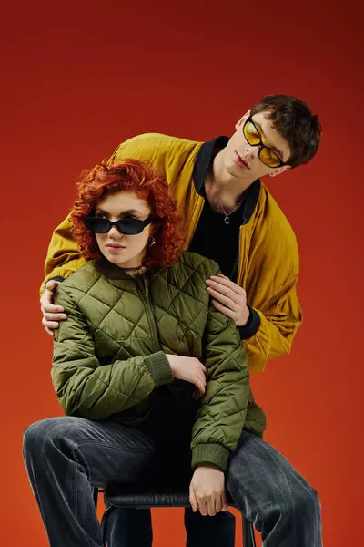 Appealing woman with red hair in sunglasses sitting on chair next to her stylish boyfriend — Stock Photo