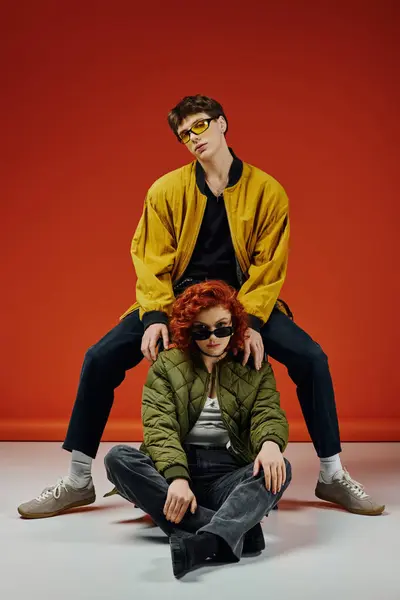 Appealing loving boyfriend sitting next to his stylish girlfriend with sunglasses on red backdrop — Stock Photo