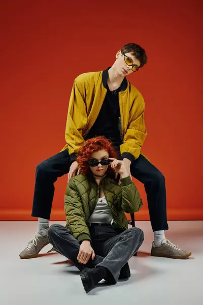 Jovem homem elegante em óculos de sol na moda posando ao lado de sua bela namorada ruiva — Fotografia de Stock