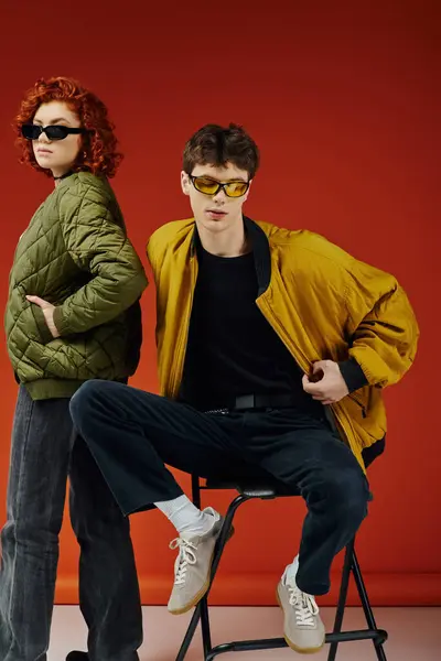 Hombre de moda de buen aspecto en gafas de sol con estilo sentado en la silla junto a su novia amorosa - foto de stock