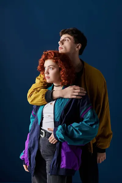Attractive fashionable couple in stylish clothes hugging lovingly and looking away on blue backdrop — Stock Photo