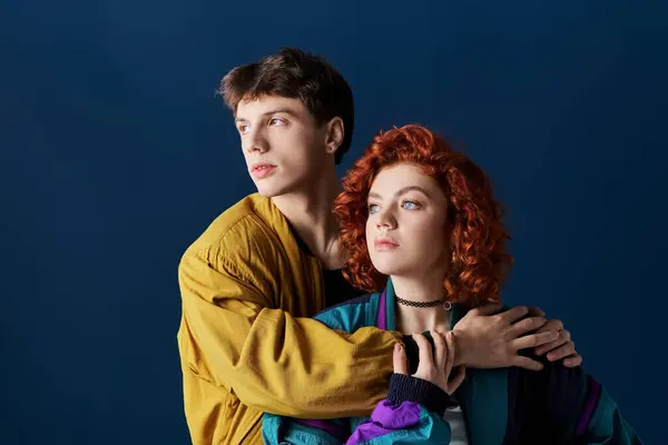 Schöne Frau und ihr Freund in lebendigen Kleidern, die sich umarmen und vor blauem Hintergrund wegschauen — Stockfoto