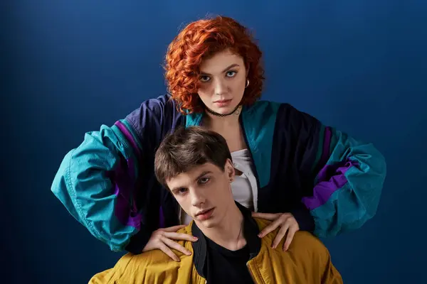 Attrayant jeune couple dans des vêtements dynamiques à la mode posant sur fond bleu et regardant la caméra — Stock Photo