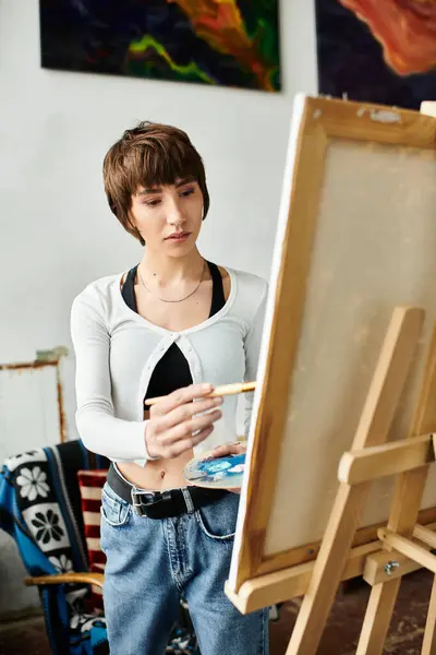 A woman stands with paintbrush by easel. — Stock Photo