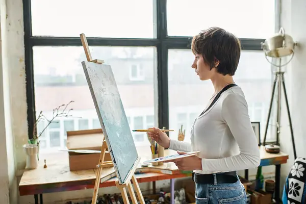 Une femme se tient en confiance devant un chevalet de peinture dans un atelier d'art. — Photo de stock