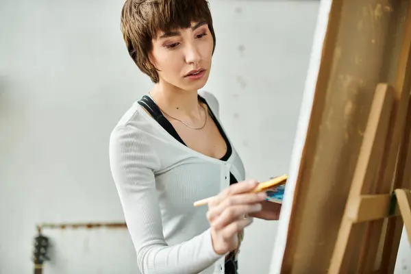 Woman stands before easel, paintbrush in hand. — Stock Photo