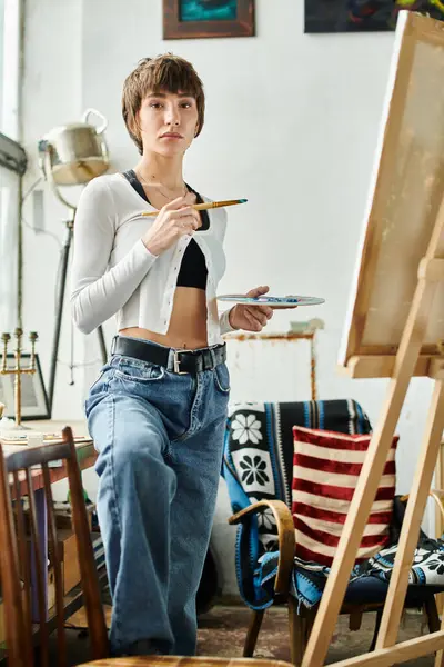 A woman holding a paintbrush, standing in front of an easel. — Stock Photo