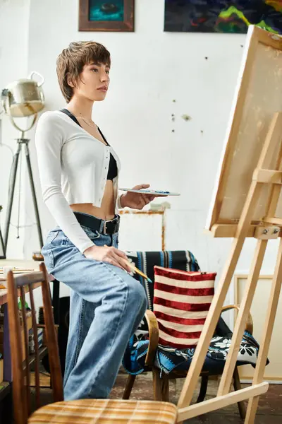 A woman seated in front of an easel, focusing on her artwork. — Stock Photo