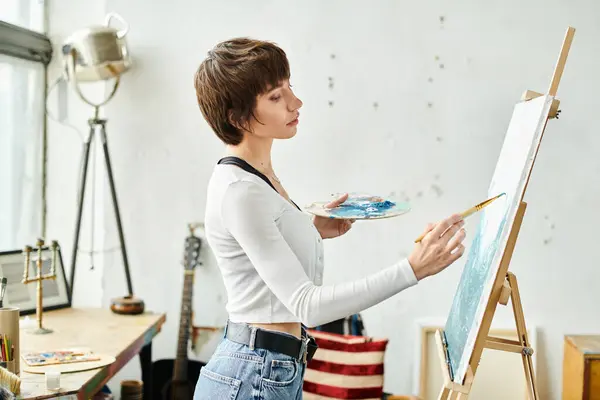 A woman in a white shirt paints on an easel. — Stock Photo