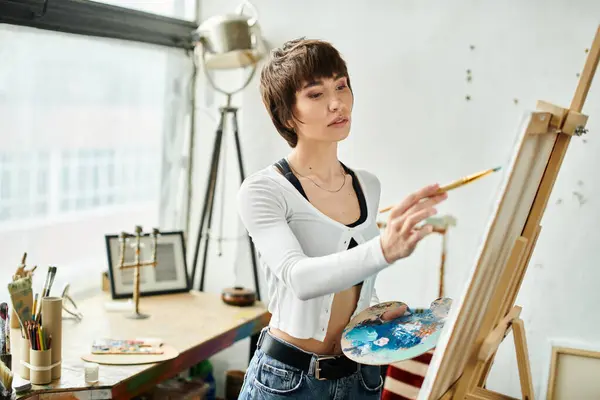 Woman in white shirt paints on easel. — Stock Photo