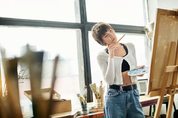 Woman creatively paints on easel, holding paintbrush. — Stock Photo