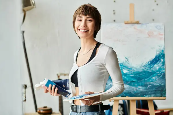 Female examines painting while holding blue paint. — Stock Photo
