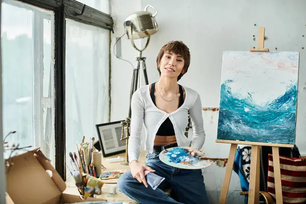 Une femme s'assoit devant une peinture, tenant délicatement une palette. — Photo de stock
