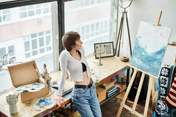 A woman stands in front of a painting on an easel, contemplatively examining the artwork. — Stock Photo