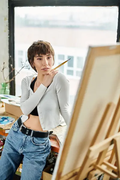 Una mujer posa frente a una pintura cautivadora, exudando gracia y estilo. - foto de stock