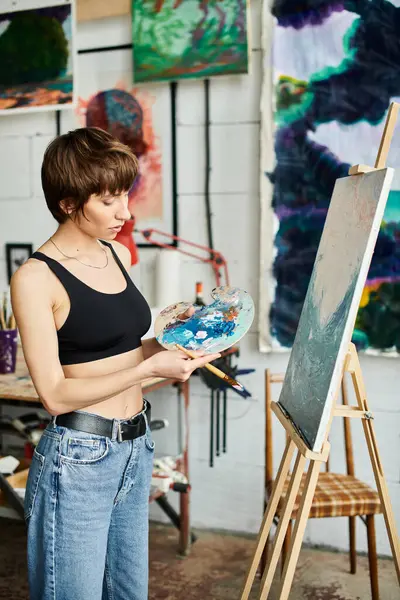Woman in black top paints with brush and palette. — Stock Photo