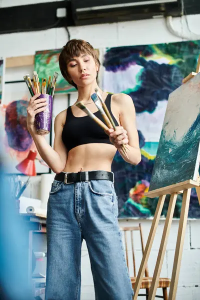 A woman in a black tank top holds paintbrushes. — Stock Photo
