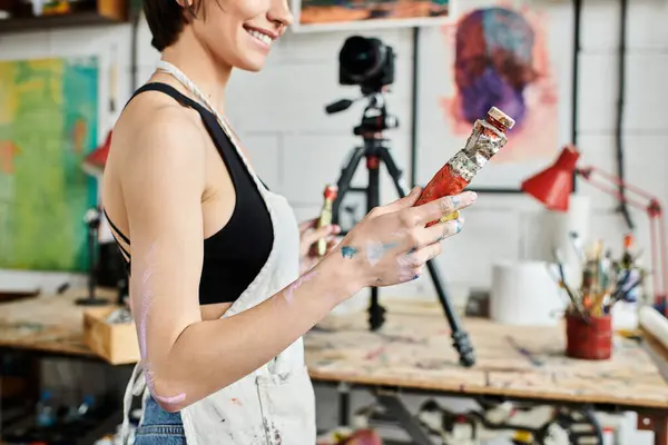 Woman holding a bottle of paint in a vibrant studio. — Stock Photo