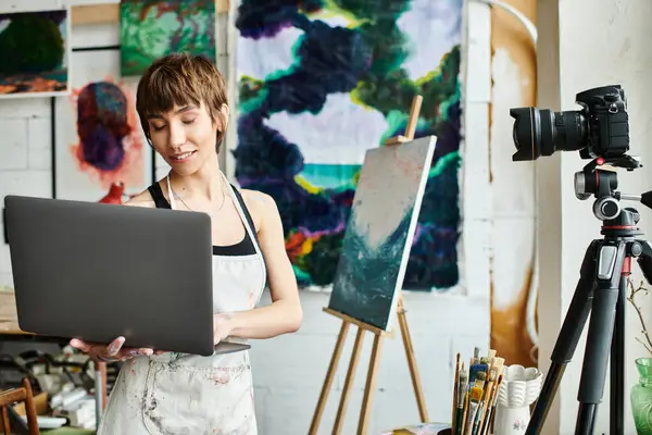 A woman holds a laptop in front of a painting. — Stock Photo