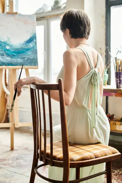 Uma mulher senta-se diante de uma pintura em uma cadeira. — Stock Photo