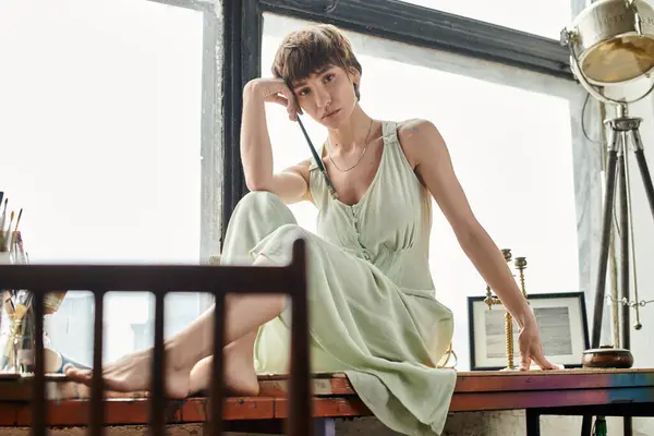 A woman in a green dress gracefully seated on a window sill. — Stock Photo