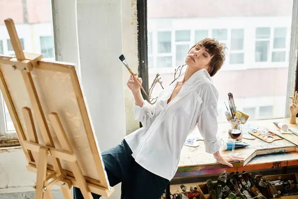 A woman holds a paintbrush while standing next to an easel. — Stock Photo