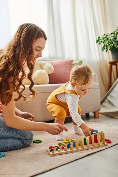 A young mother happily playing with her toddler daughter on the floor in their cozy home. — Stock Photo