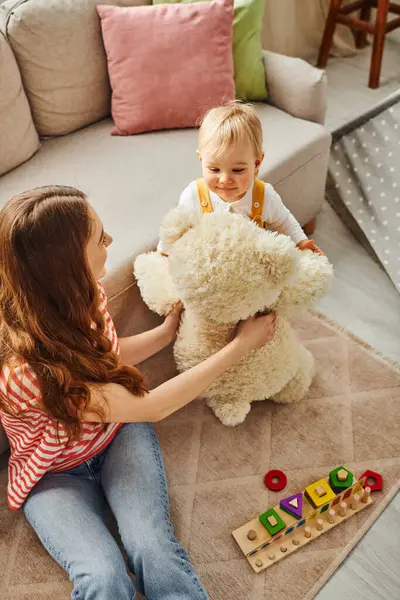 Uma jovem mãe e sua filha criança alegremente brincando com um urso de pelúcia, compartilhando alegria e criando memórias ao longo da vida. — Fotografia de Stock