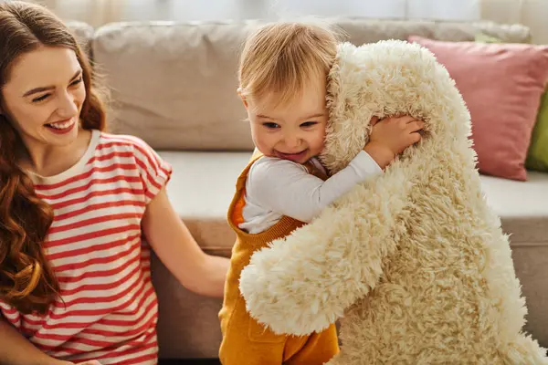 A young mother tenderly holds her baby while embracing a teddy bear in a heartwarming display of love at home. — Stock Photo